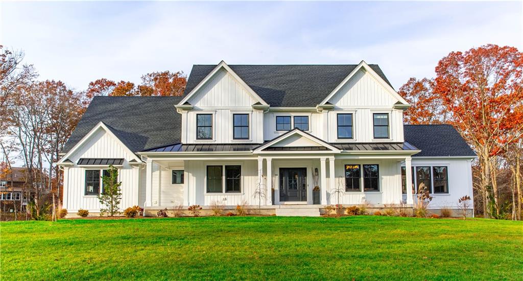 White board-and-batten modern farmhouse on a manicured lawn surrounded by autumn foliage